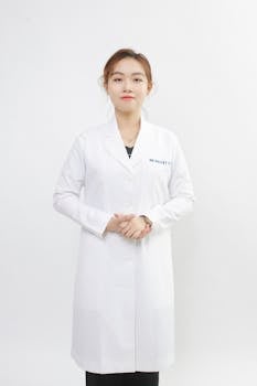 Portrait of a confident female doctor in a white coat, standing against a plain background.