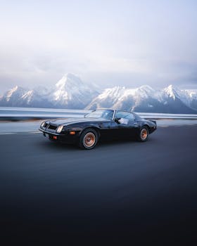 A vintage sports car speeds along a road with stunning snowy mountains in the background, exuding adventure