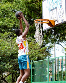 Dynamic shot of a basketball player dunking in an outdoor court surrounded by greenery.
